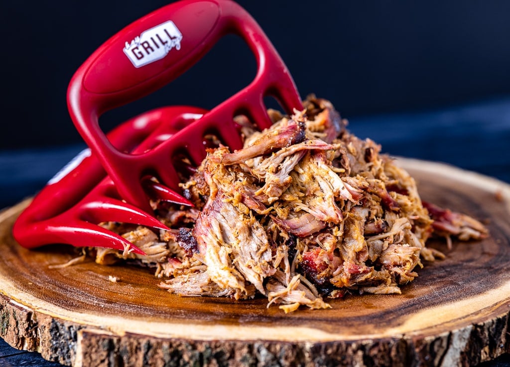 Meat shredder claws in shredded pulled pork on a wooden board.